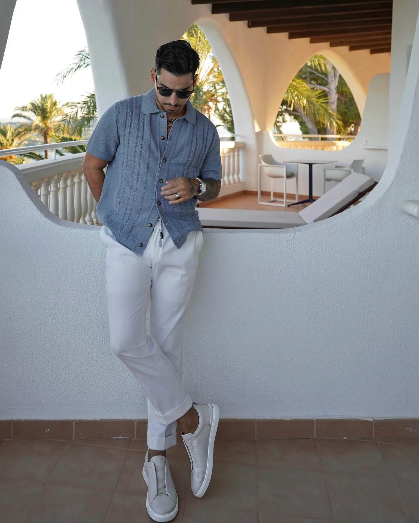 Rob on a white terrace in Mallorca, in a blue knit shirt and white trousers