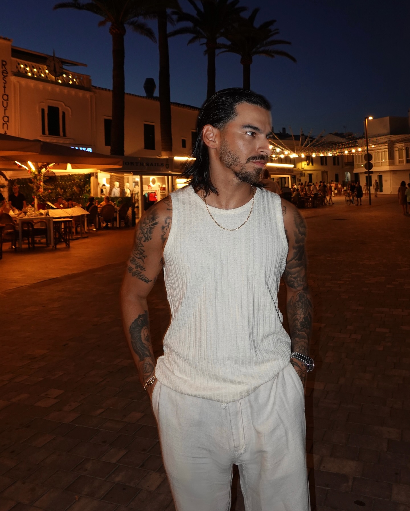Rob in Menorca at night, wearing a white tank and white trousers